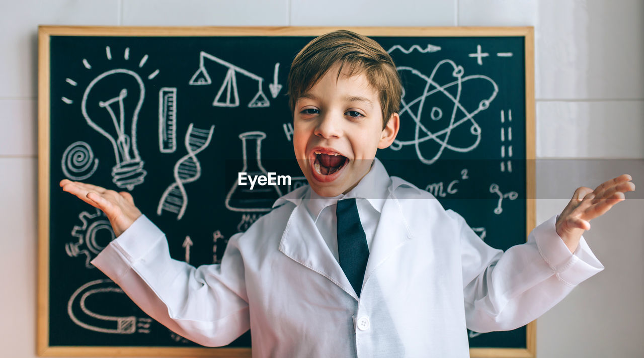 Portrait of cute boy standing against blackboard in classroom