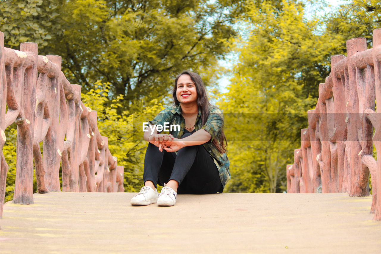 Portrait of smiling young woman sitting on bridge