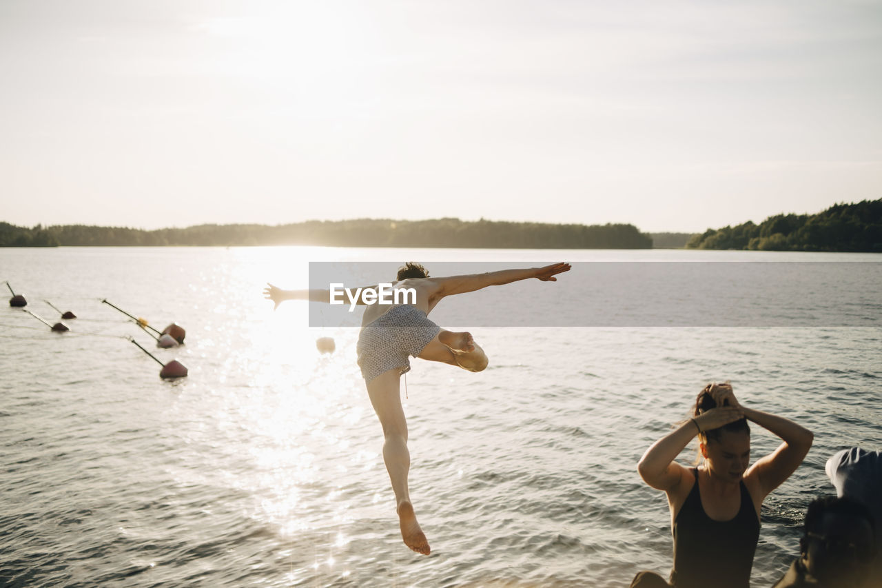 Shirtless man diving from jetty at lake against sky in summer