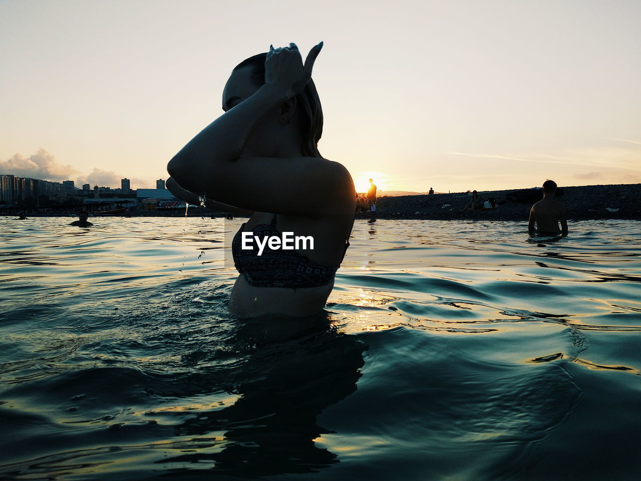 Woman standing in swimming pool against sky during sunset