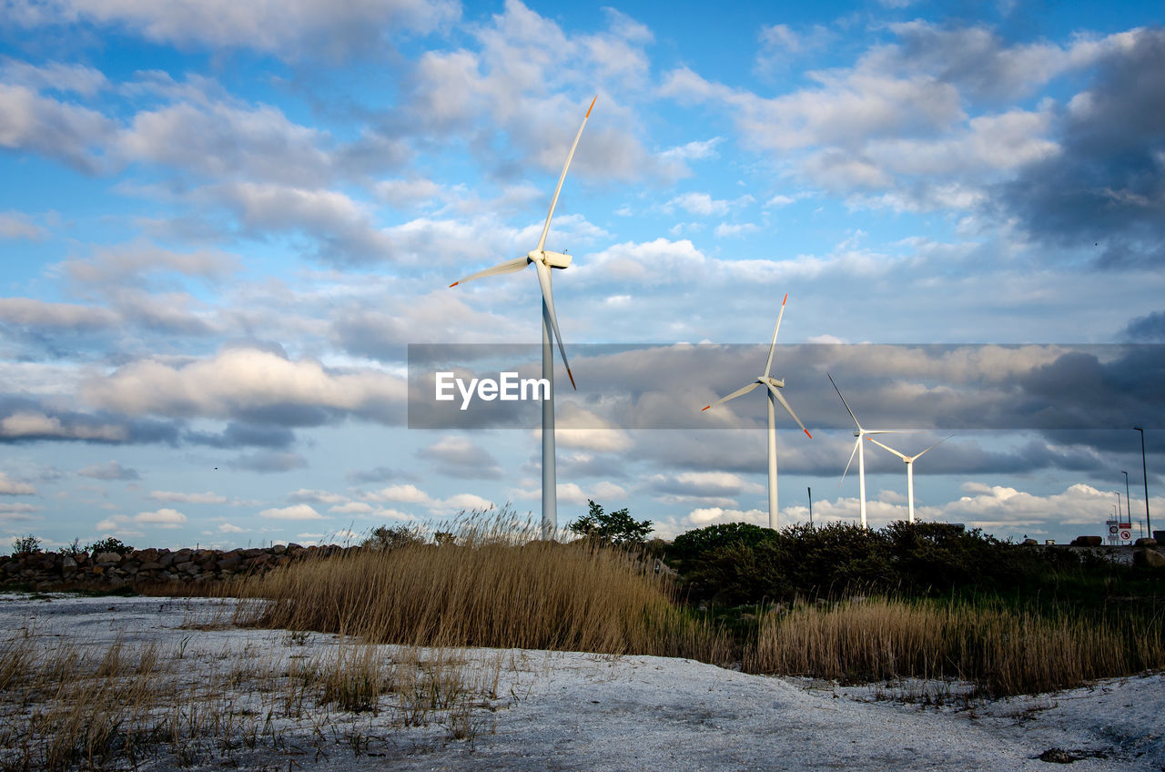 WINDMILLS ON FIELD AGAINST SKY