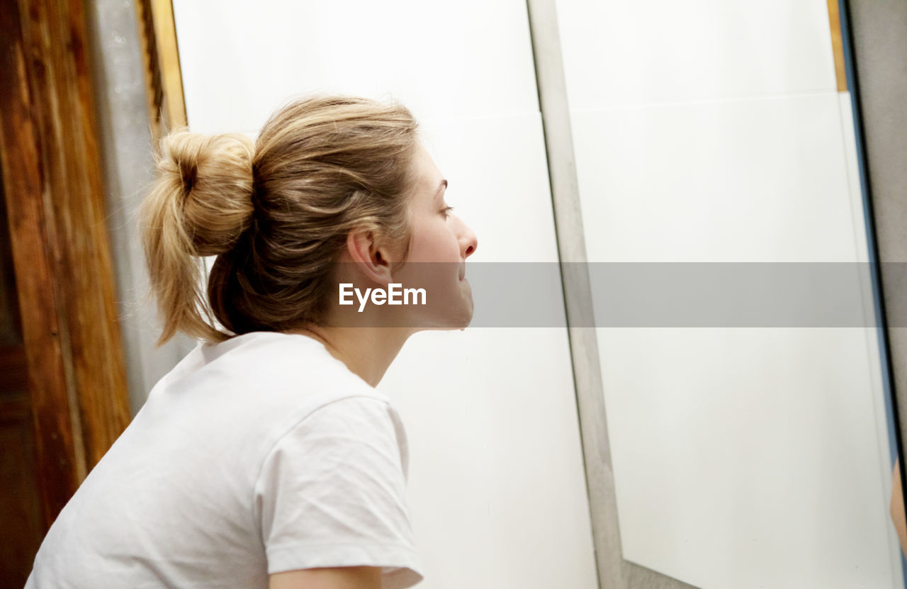 Side view of woman washing her face in bathroom looking at camera