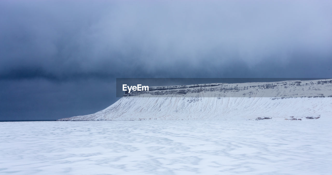 Frosted icelandic fjords with scenic mountain top in the background with storm cloud in the sky