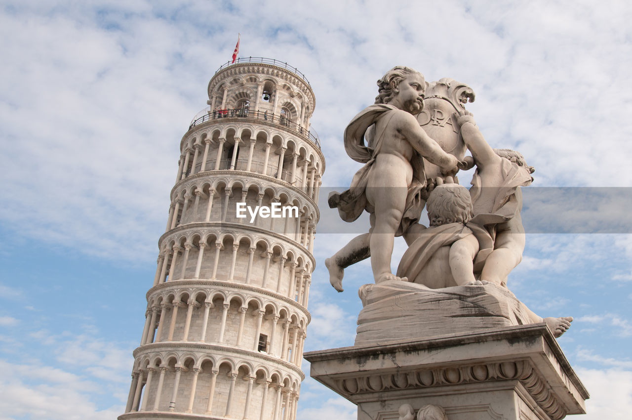 Statues by leaning tower of pisa against sky