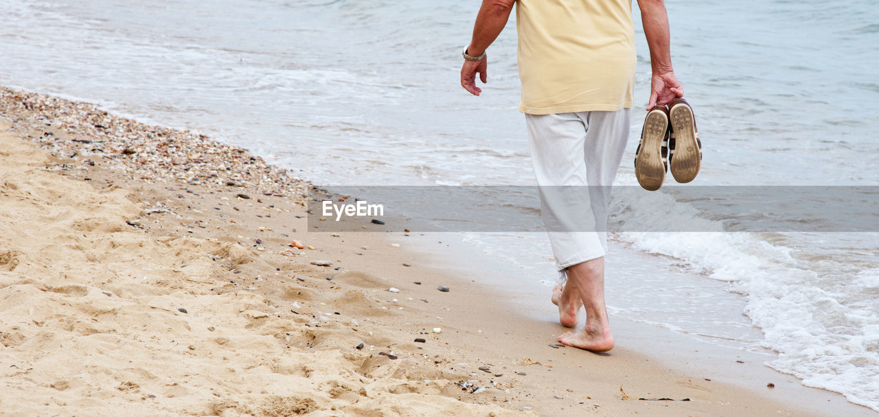 Low section of man walking at beach