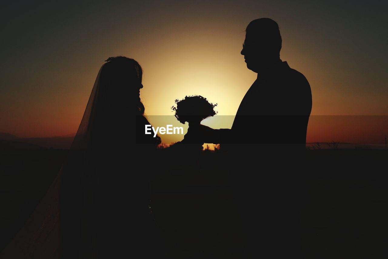 SILHOUETTE COUPLE STANDING AGAINST ORANGE SKY