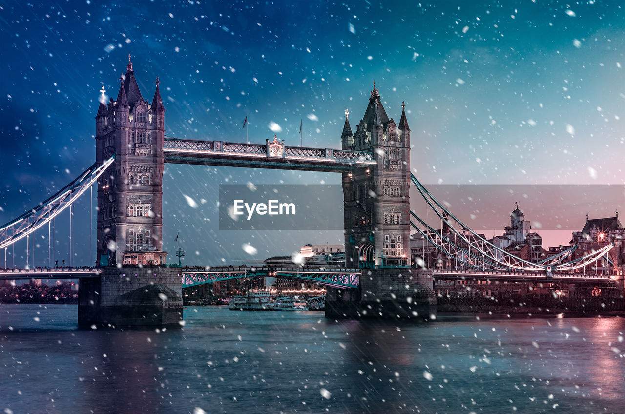 Tower bridge over river against blue sky during snowfall