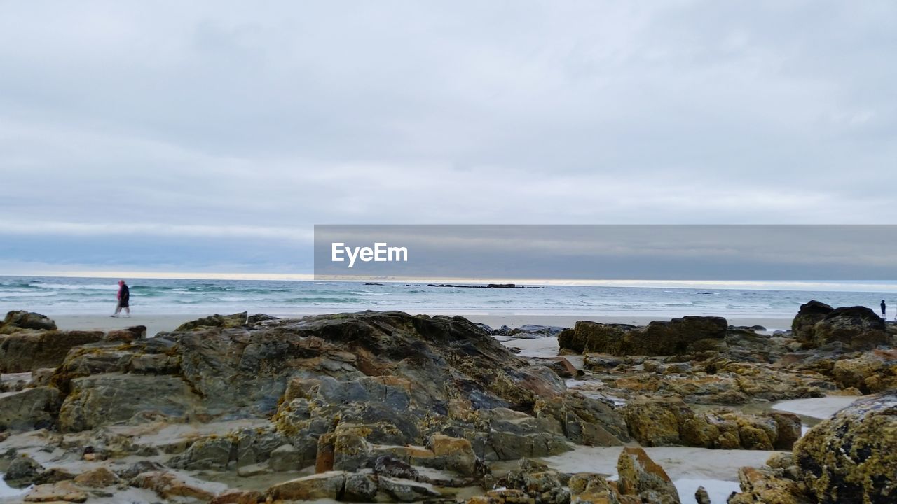 People walking on beach against cloudy sky