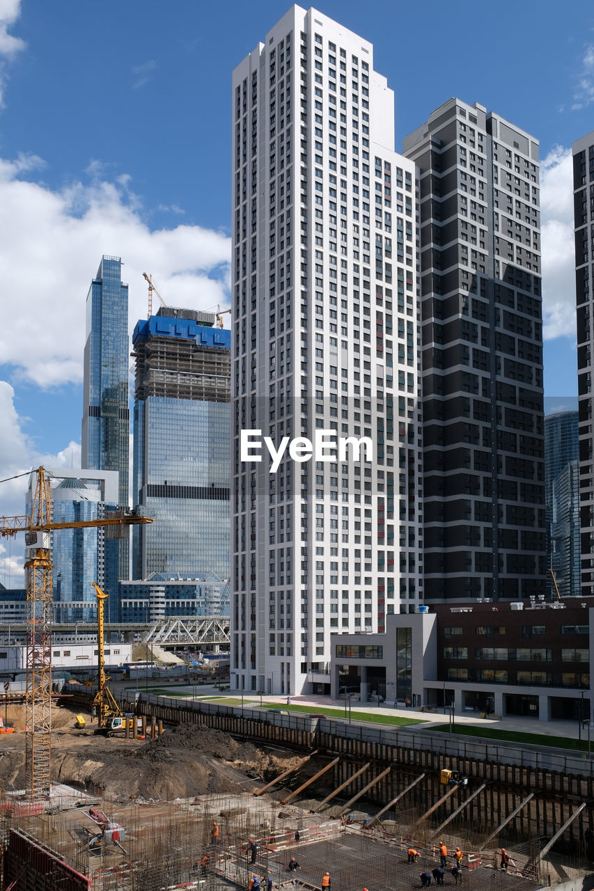 Construction site with foundation pit, machinery and worcers near of city skyscrapers