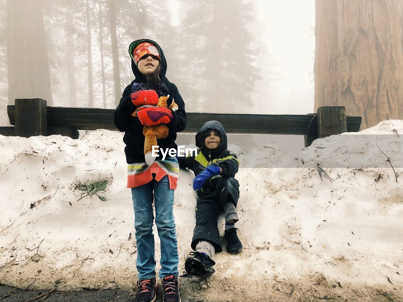 Portrait of cute siblings on snow covered field during winter