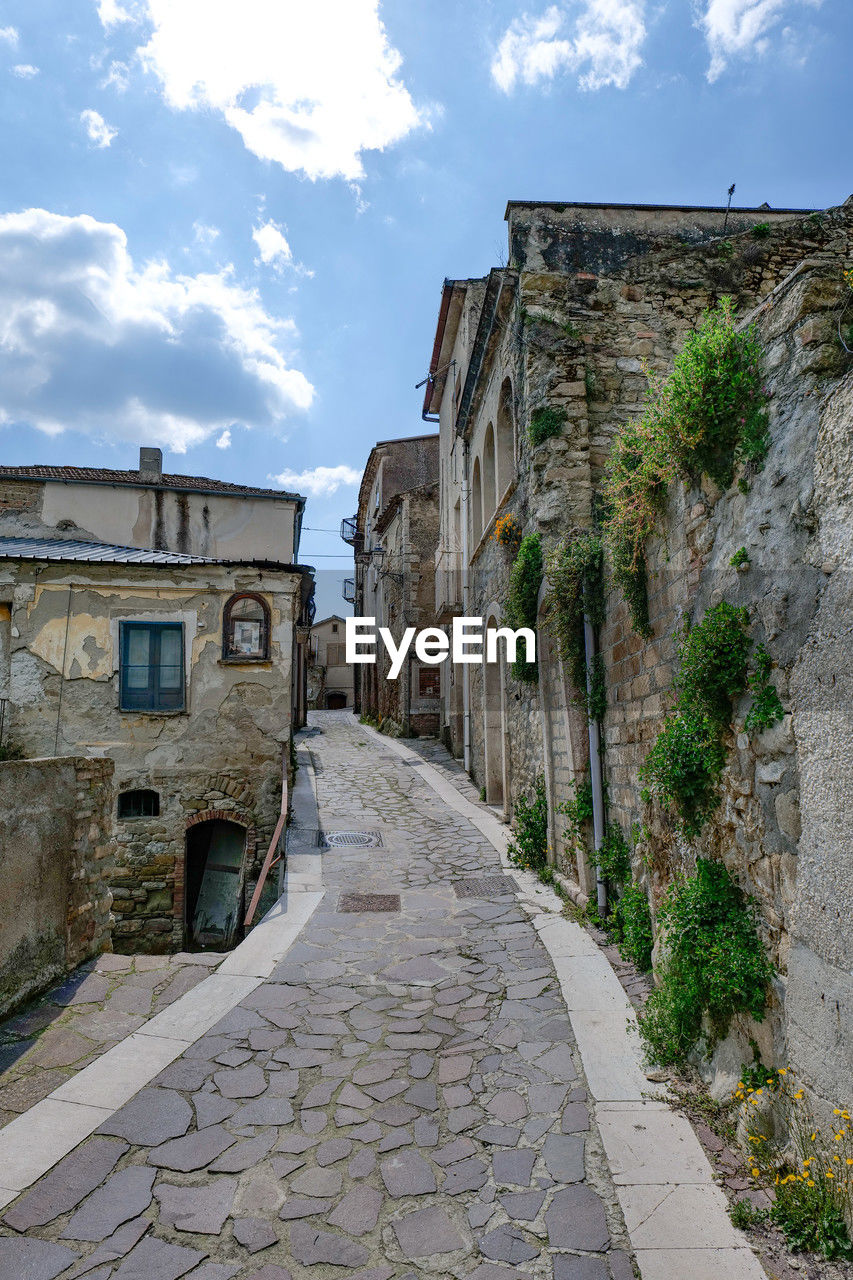architecture, town, building exterior, built structure, sky, village, building, city, wall, cloud, cobblestone, street, history, nature, footpath, the past, travel destinations, alley, road, residential district, no people, old, the way forward, house, ancient history, waterway, travel, neighbourhood, outdoors, stone material, tourism, estate, ruins, wall - building feature, day, fortification, medieval, paving stone, blue, stone wall, ancient