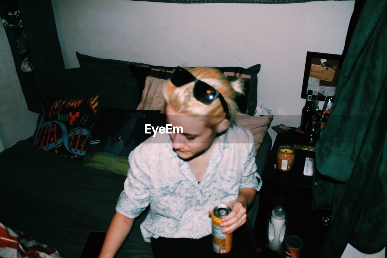 High angle view of young woman sitting with drink can on bed at home