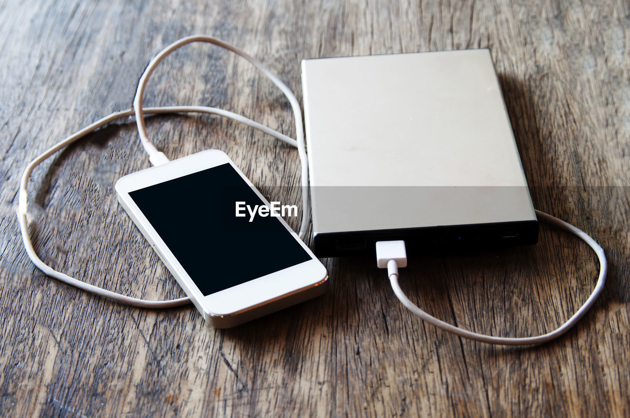 High angle view of mobile phone with powerbank on wooden table