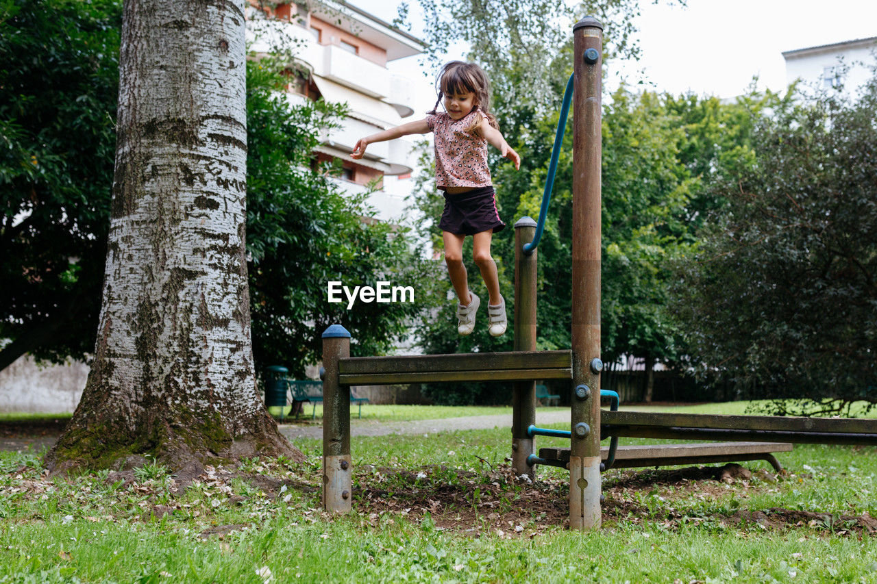 Happy little girl jumping from the wooden bench in the park