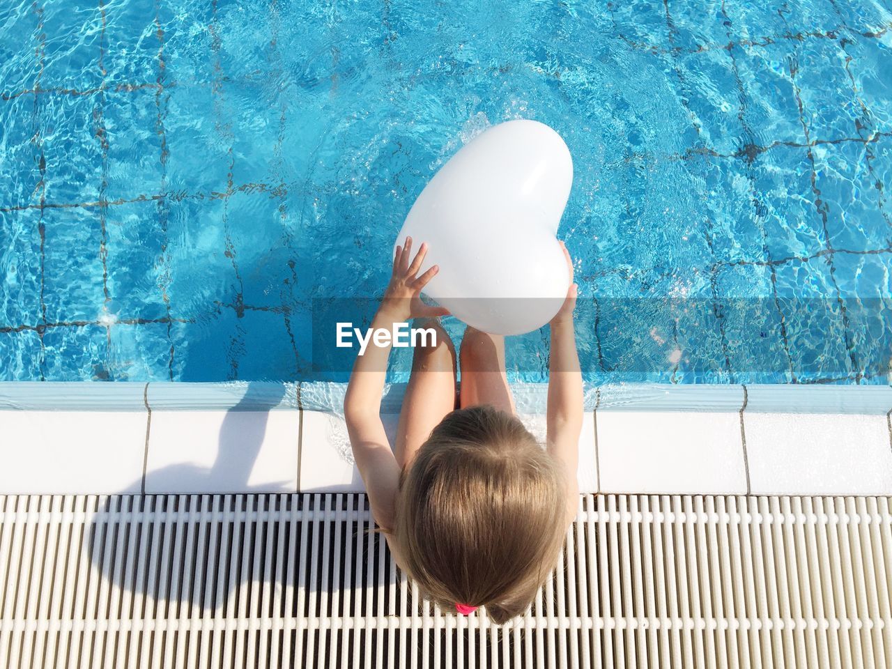 Directly above shot of girl holding balloon while sitting by poolside