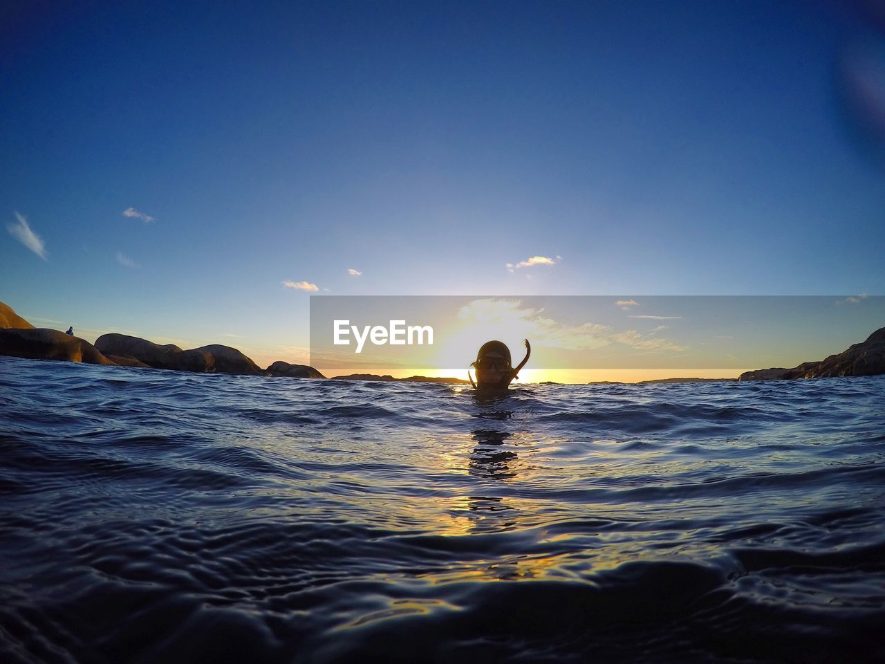 Person swimming in sea against sky during sunset