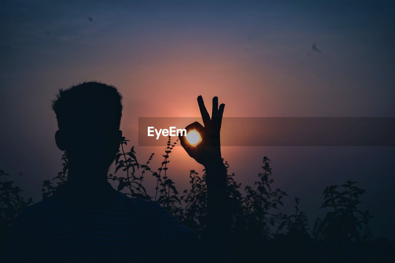 Optical illusion of silhouette mature man holding sun against sky during sunset