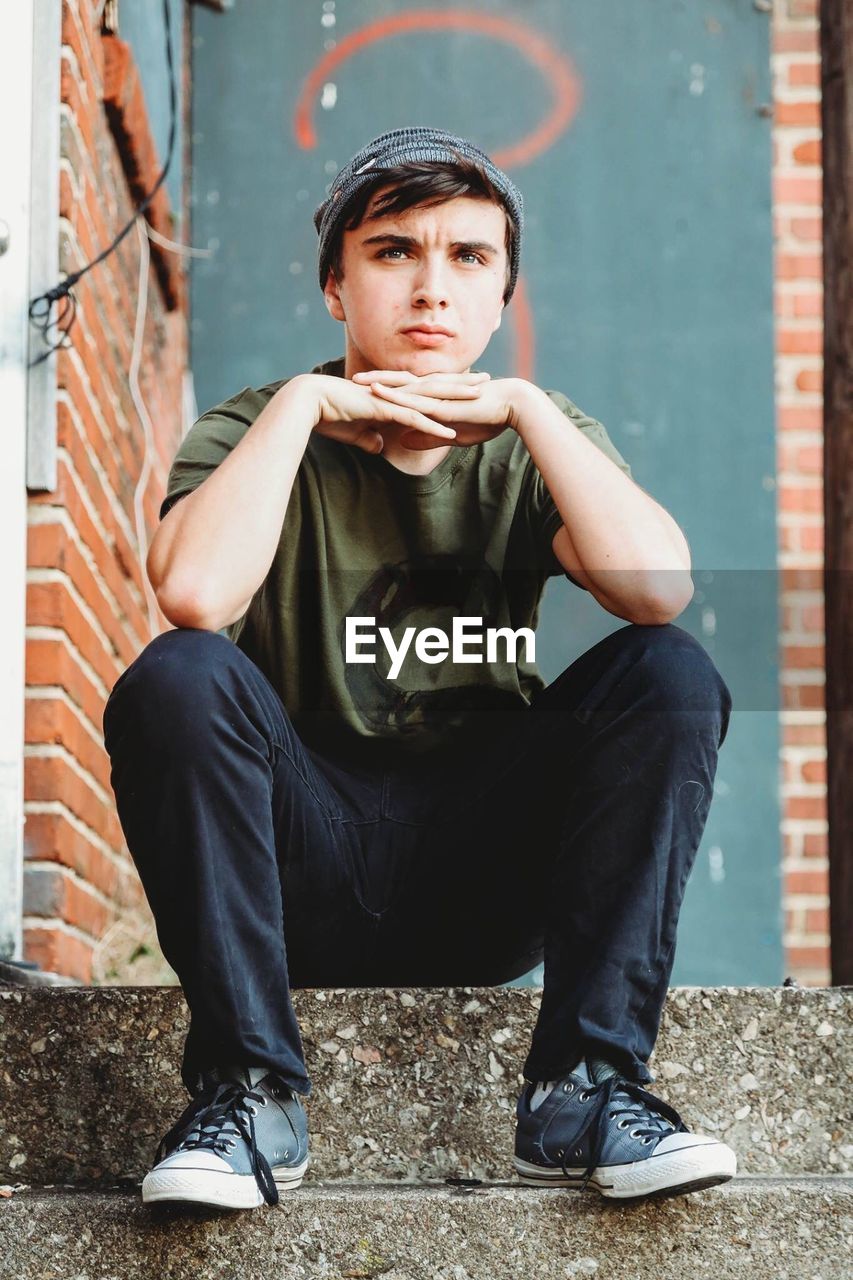 Portrait of teenage boy sitting on steps against wall