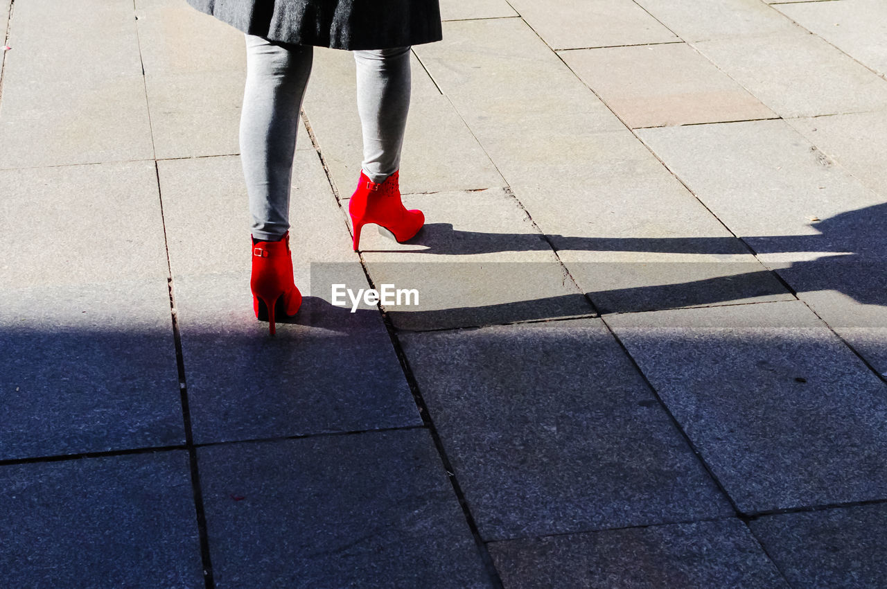 Low section of woman in red high heels walking on walkway