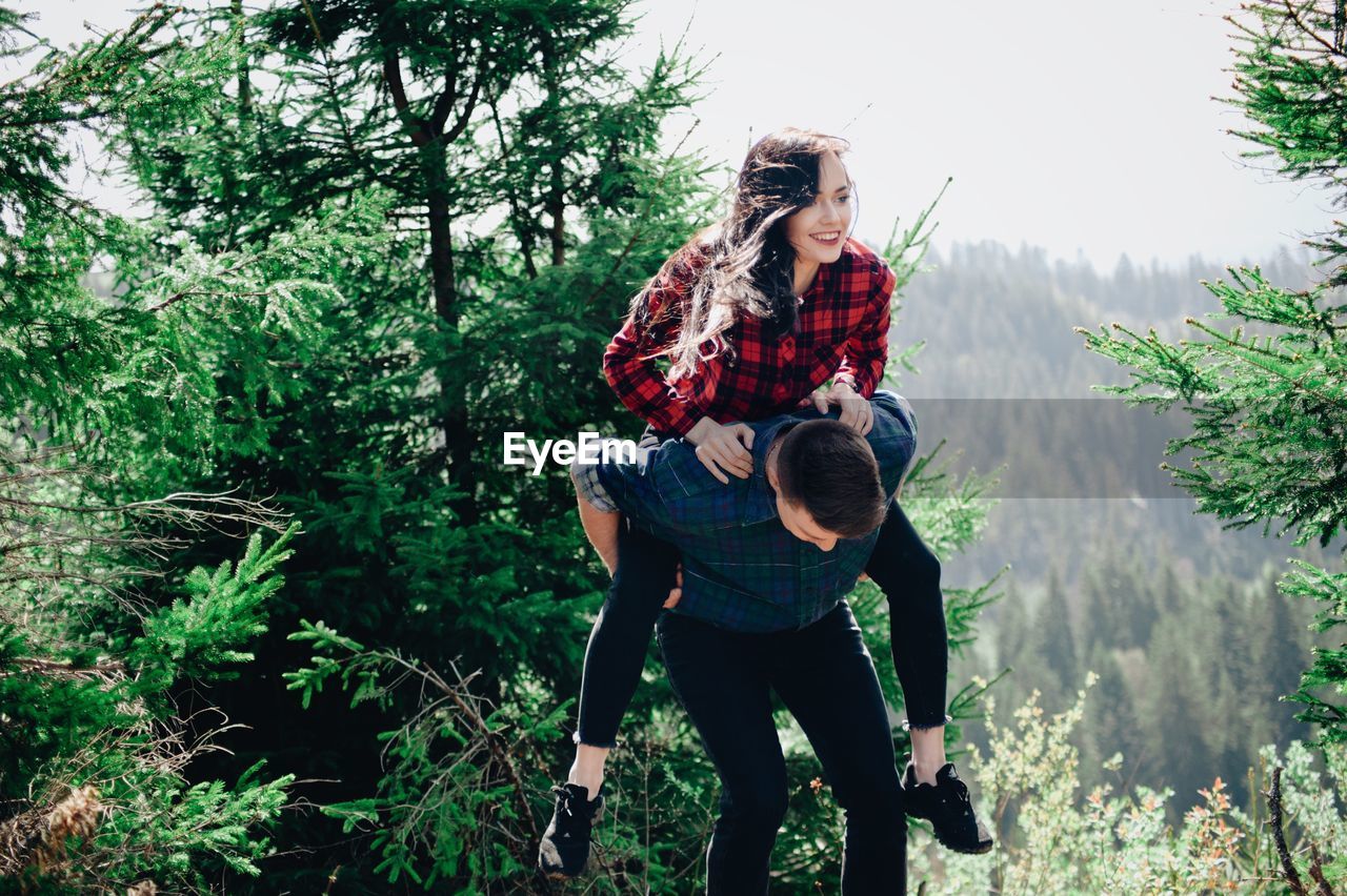 Boyfriend piggybacking smiling girlfriend in forest