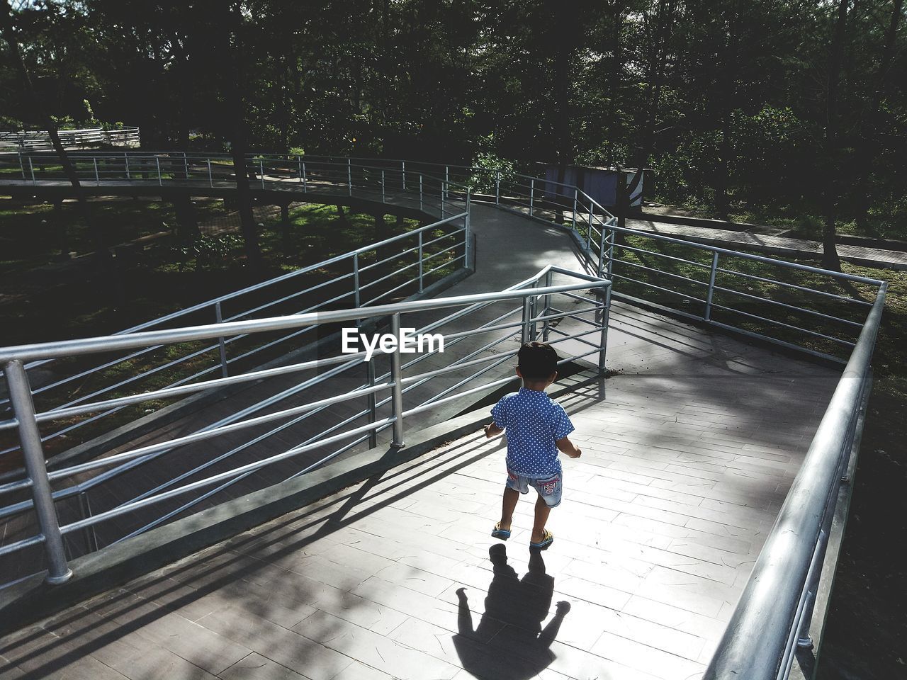 Rear view of boy walking on footbridge during sunny day