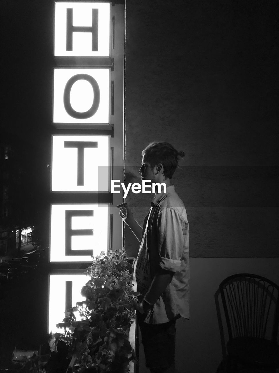 Side view of young man smoking by illuminated sign