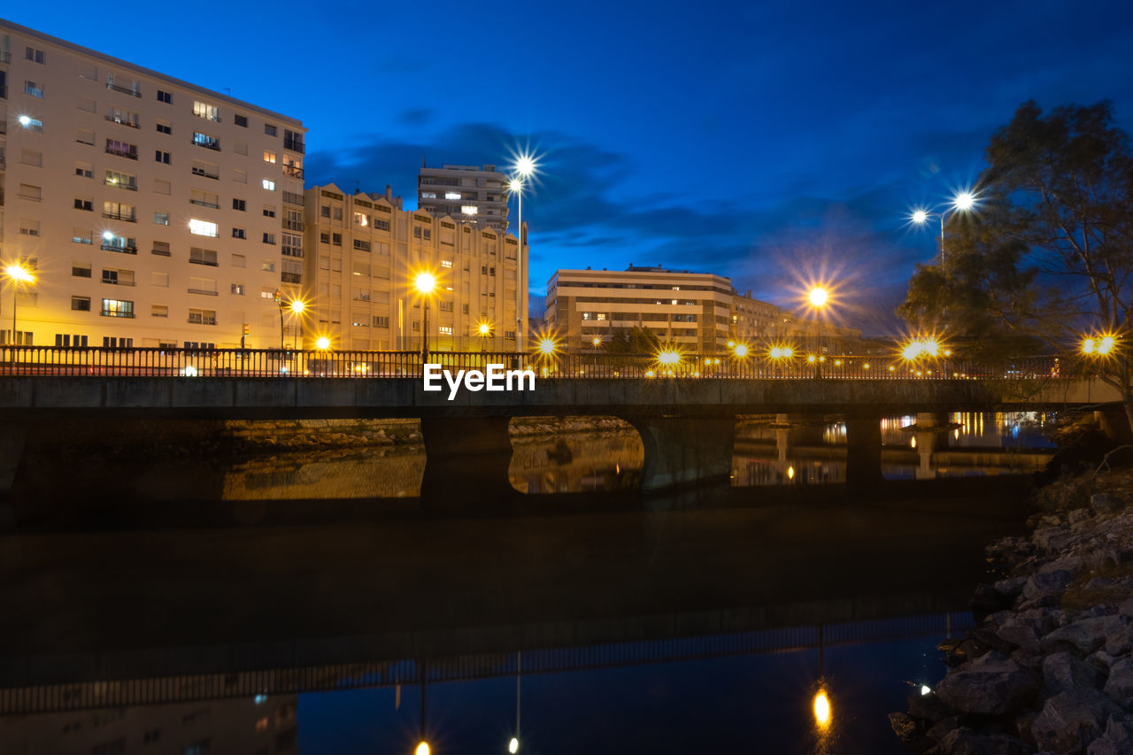 Illuminated bridge over canal by buildings against sky at night