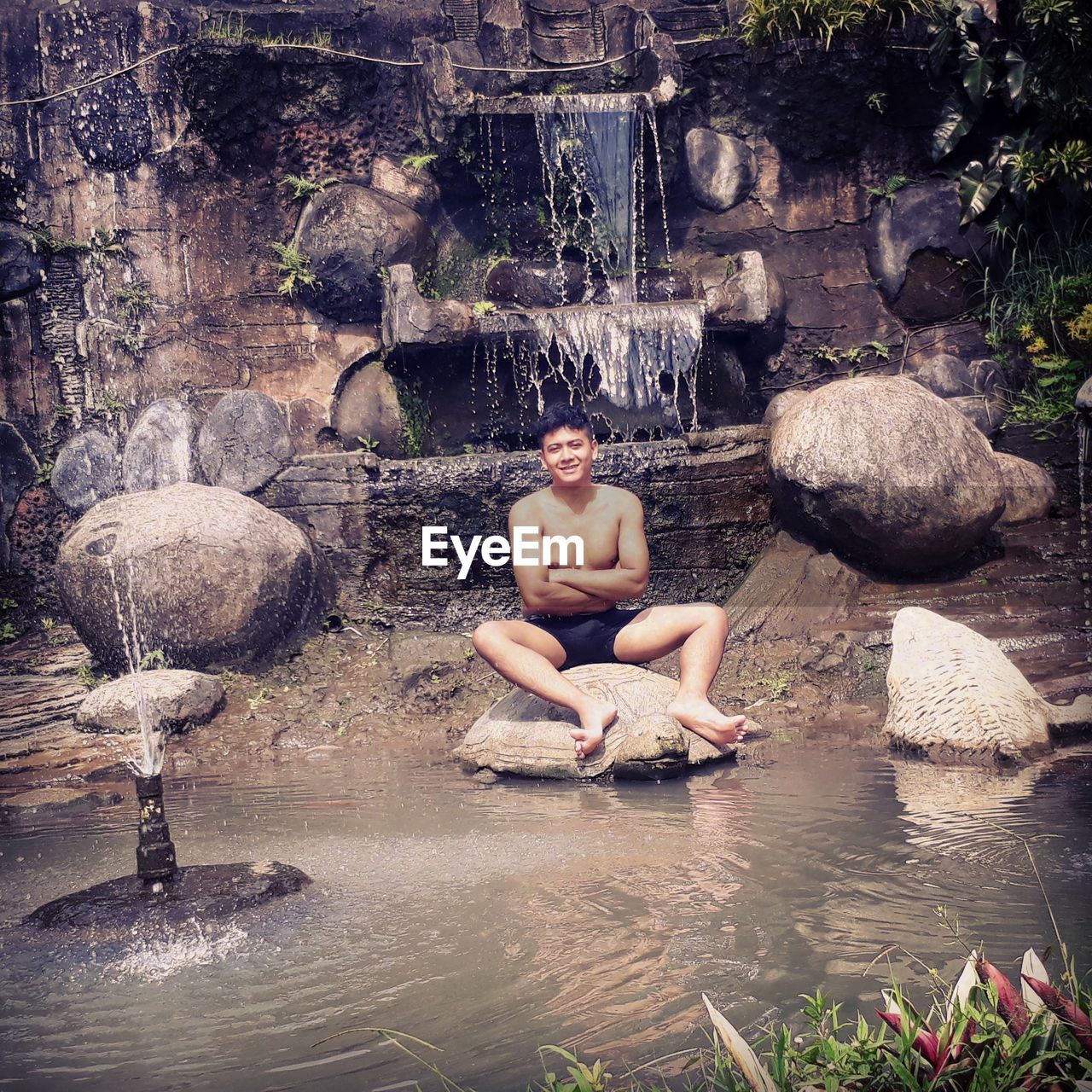 Shirtless young man sitting on rock