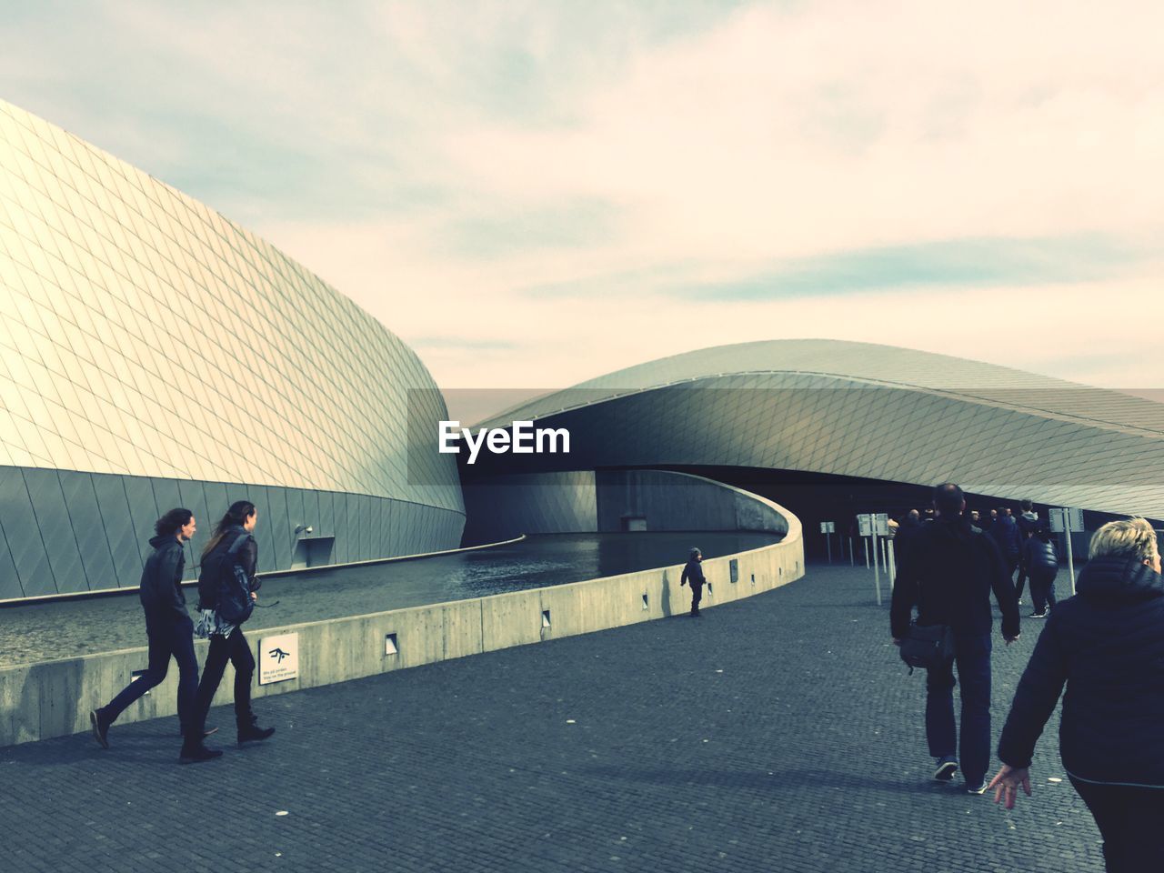 People walking at modern building against sky