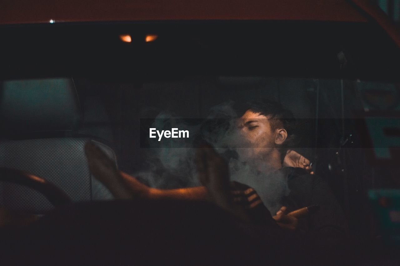 Man exhaling smoke in car at night