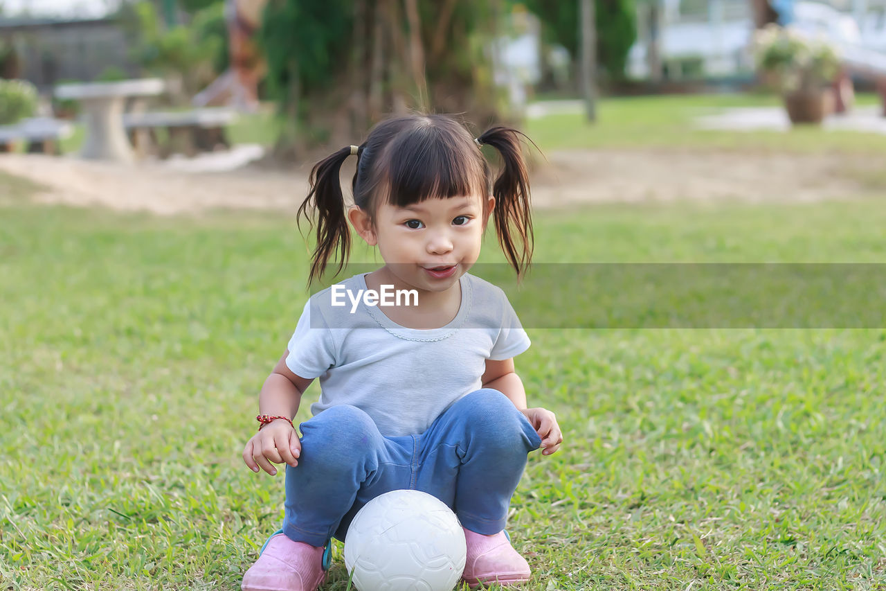 Portrait of cute girl sitting by ball at park