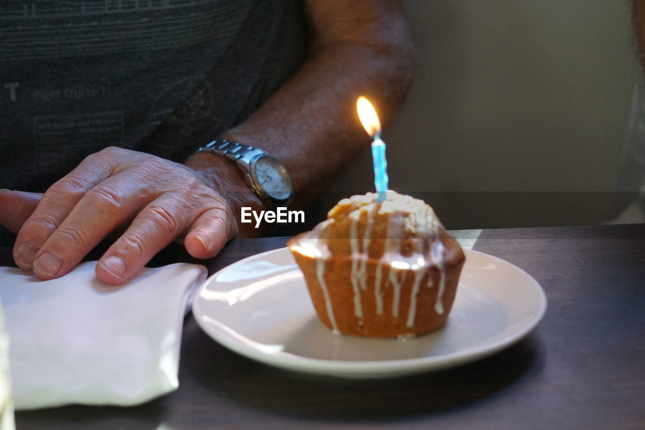 Midsection of man by illuminated candle on cake over table