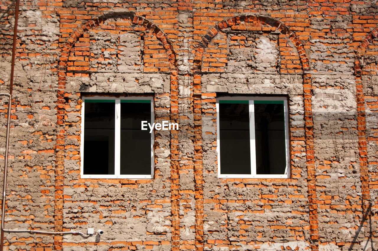 Unplastered brick wall of a building with two windows.