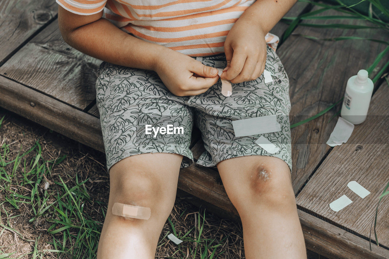 Close-up of child's leg injury. injured his knee. boy puts band-aid on wound after falling in street