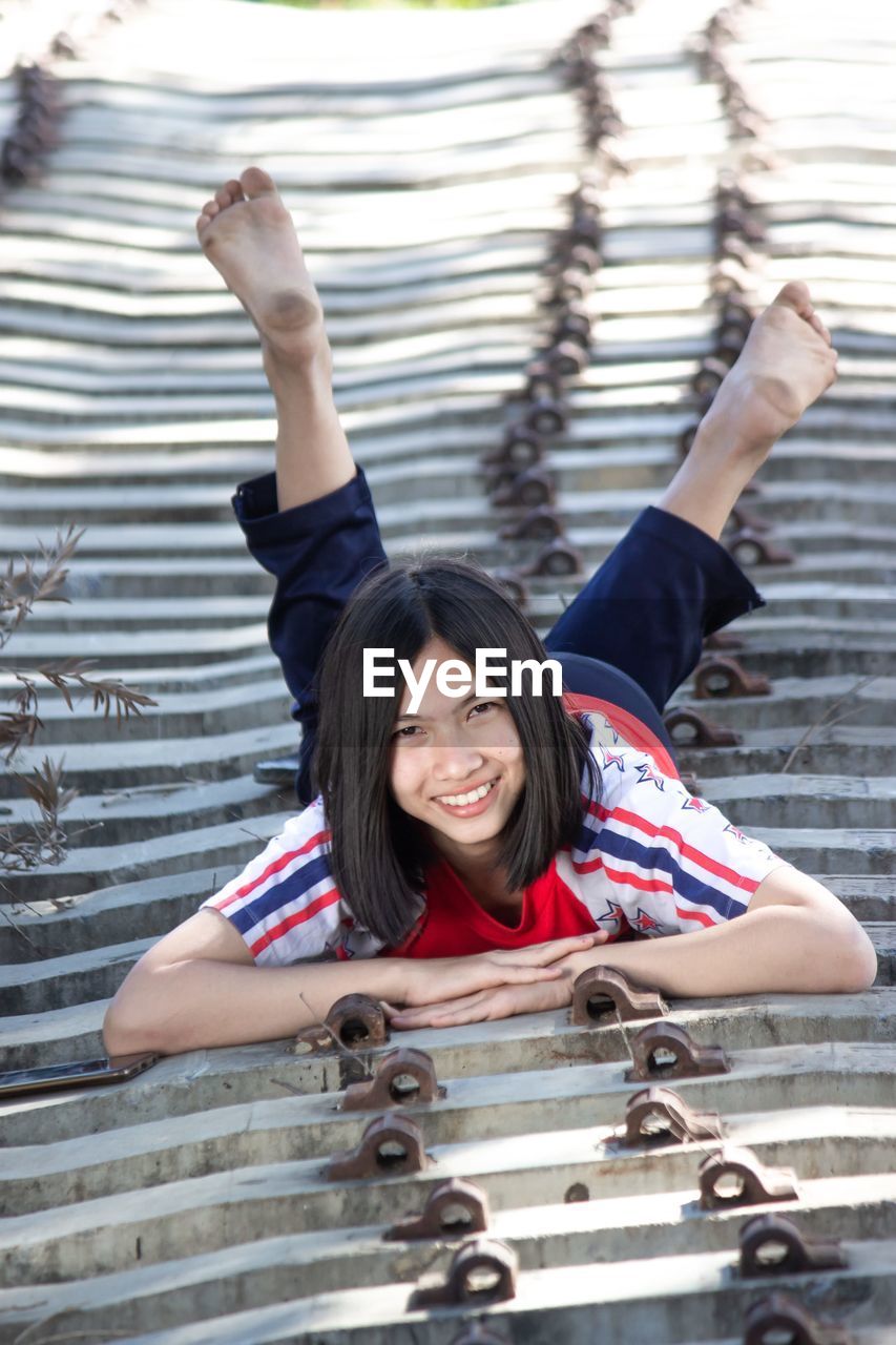 PORTRAIT OF A SMILING YOUNG WOMAN WITH ARMS RAISED