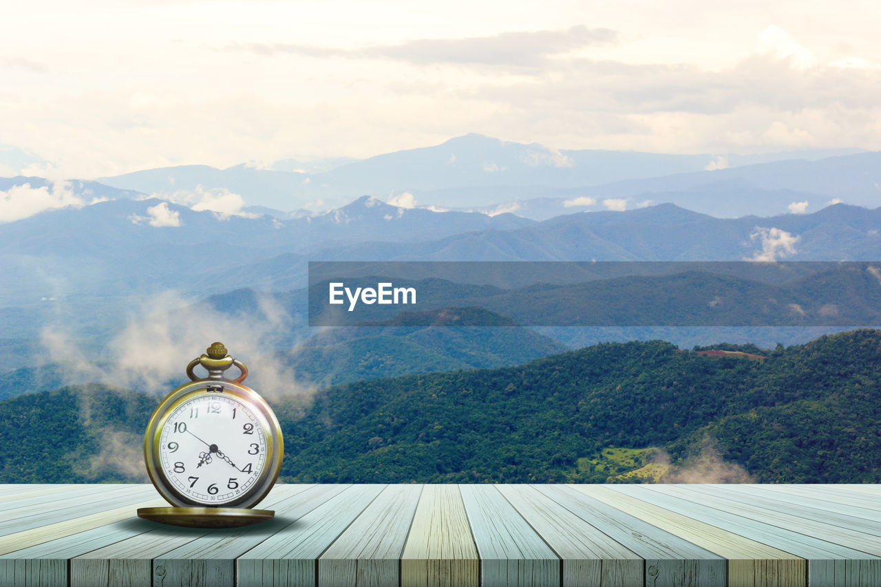 CLOCK AMIDST TREES AGAINST MOUNTAINS