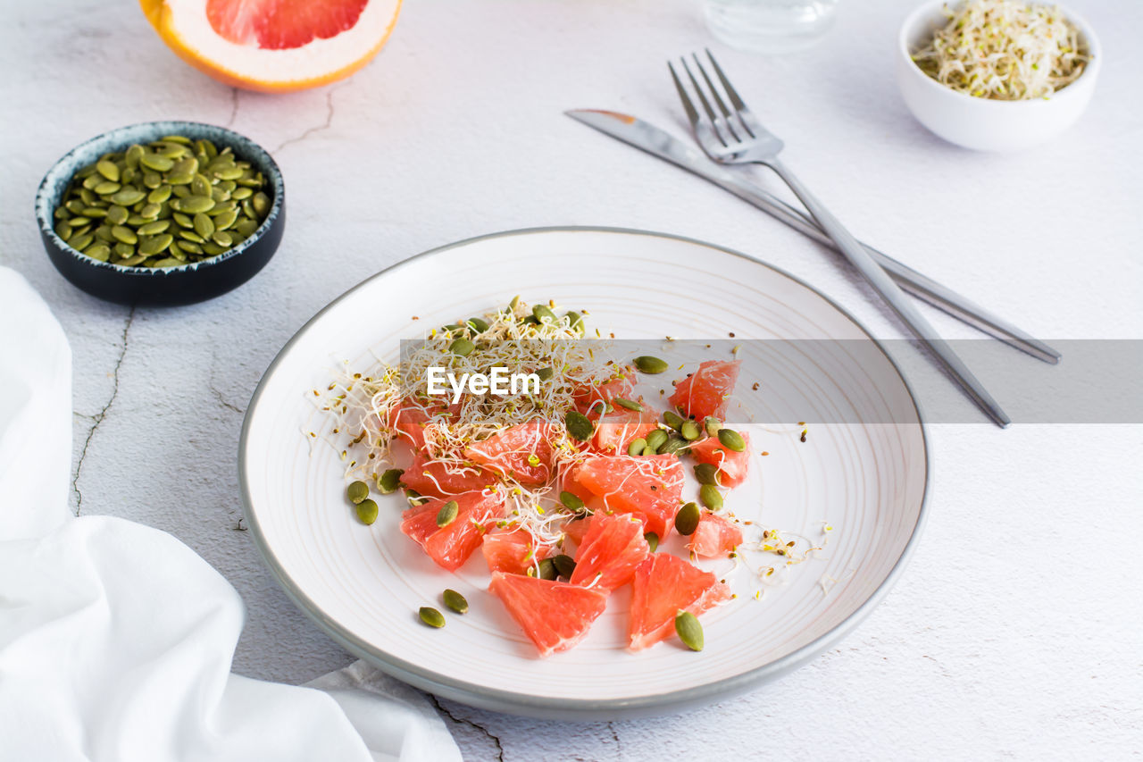 Fresh salad of grapefruit, clover and alfalfa sprouts and pumpkin seeds and cutlery on a plate 