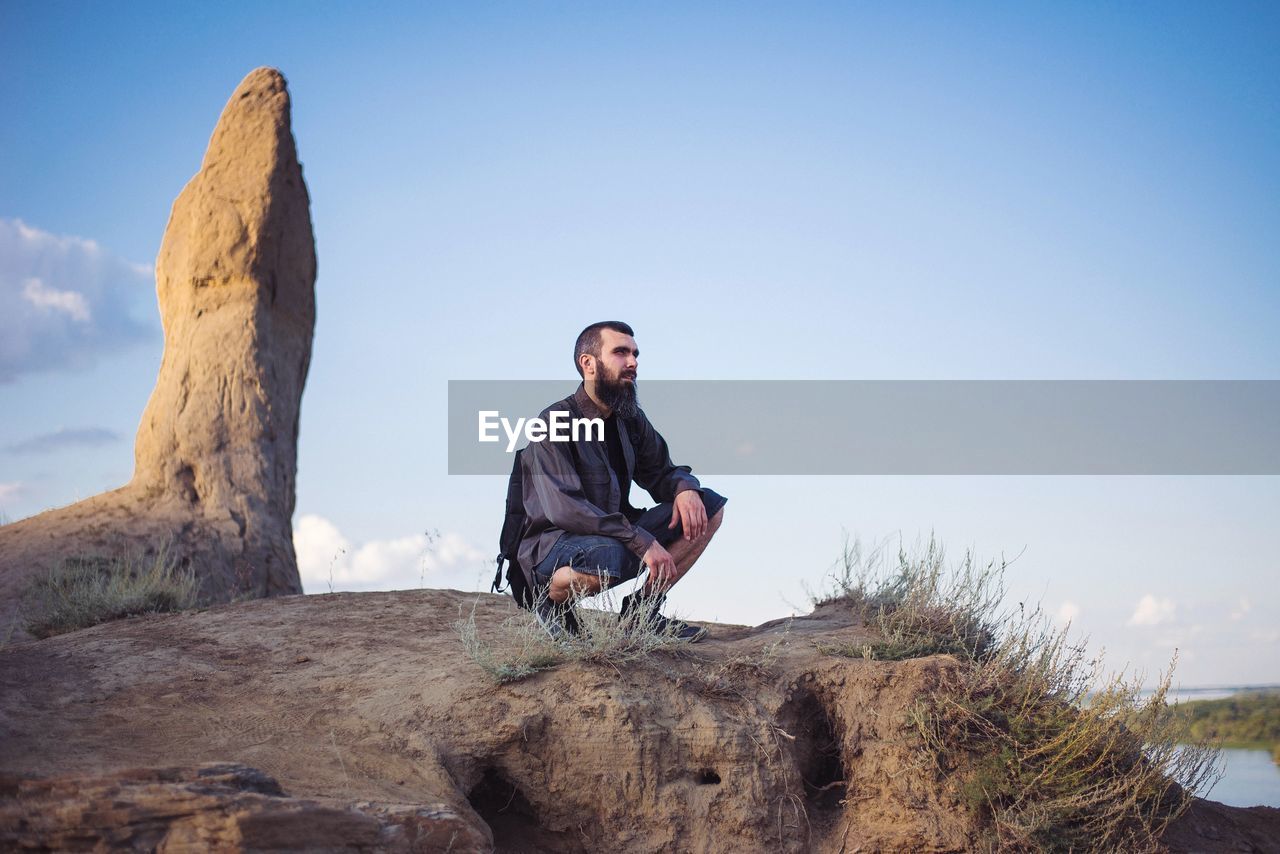 Brutal man against the background of the sky and sandy mountains