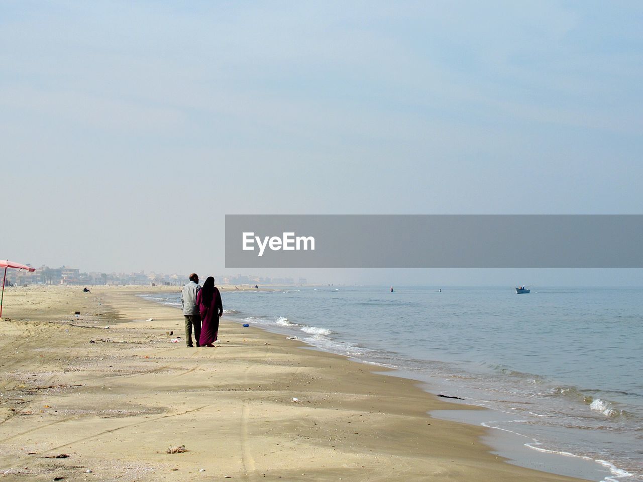 Rear view of couple walking at beach against sky