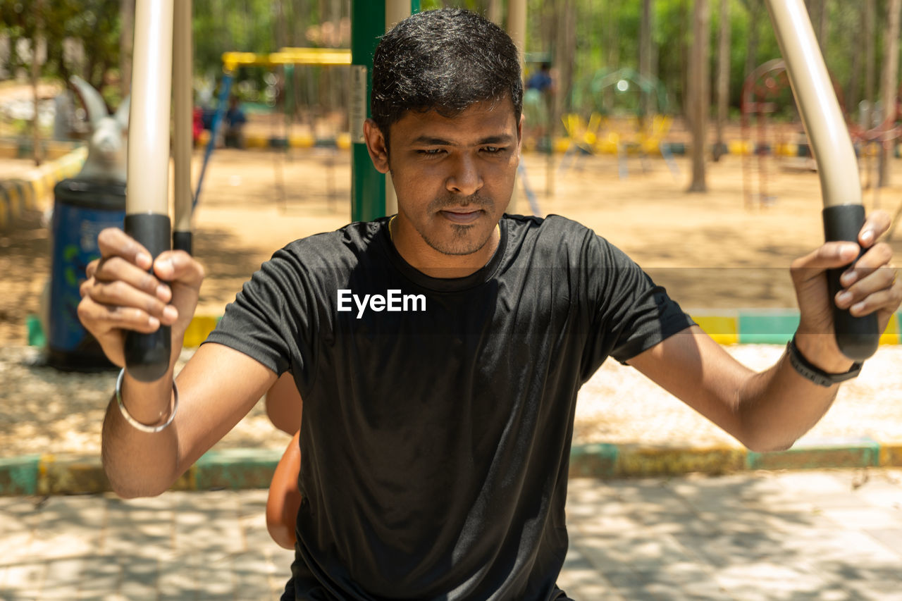 one person, sports, lifestyles, men, adult, exercising, strength, muscular build, activity, sports training, holding, leisure activity, person, physical fitness, vitality, outdoors, front view, relaxation, waist up, nature, portrait, young adult, playground, athlete, motion, focus on foreground, determination, recreation