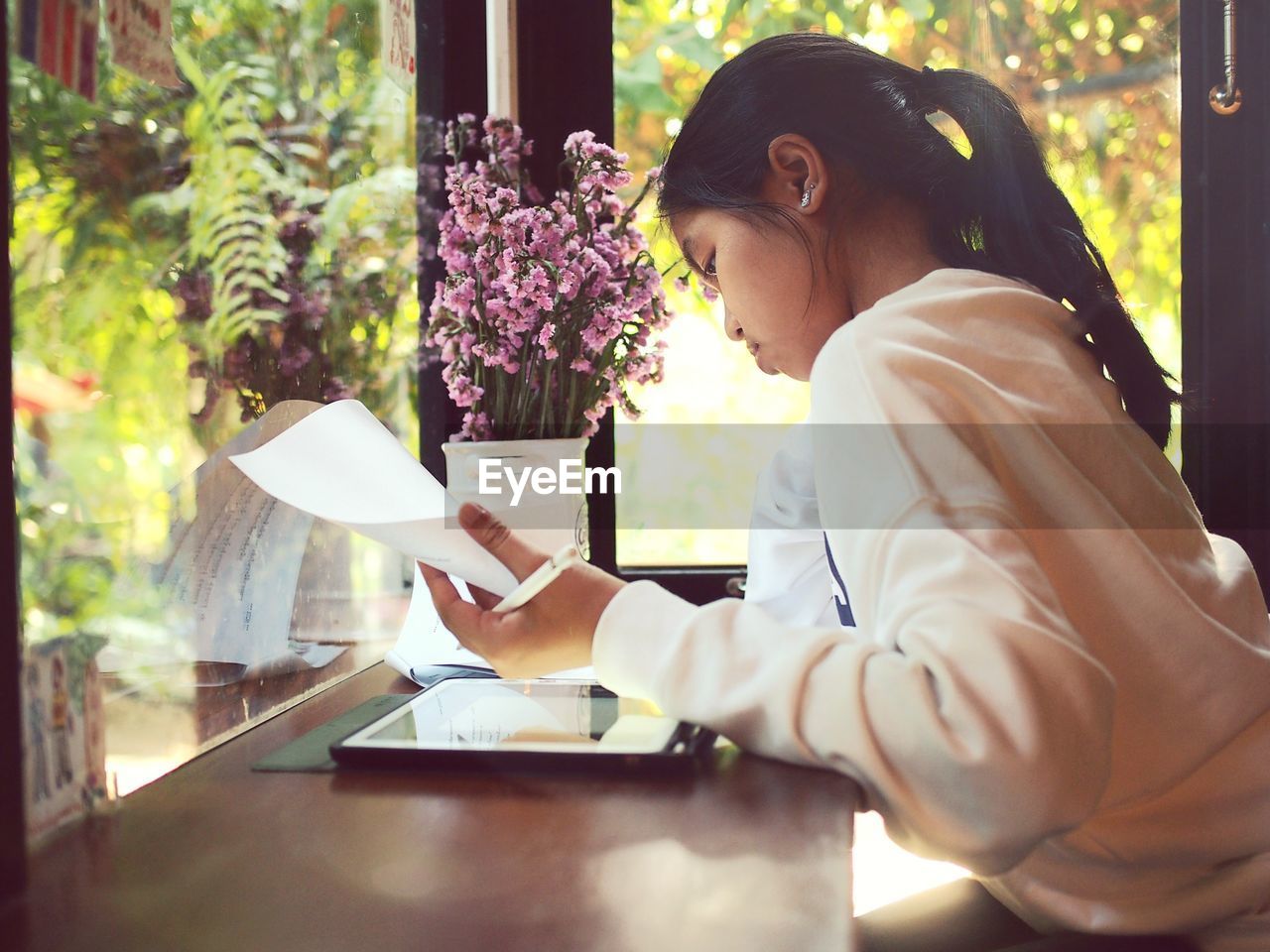 Side view of teenage girl using digital tablet at table against window