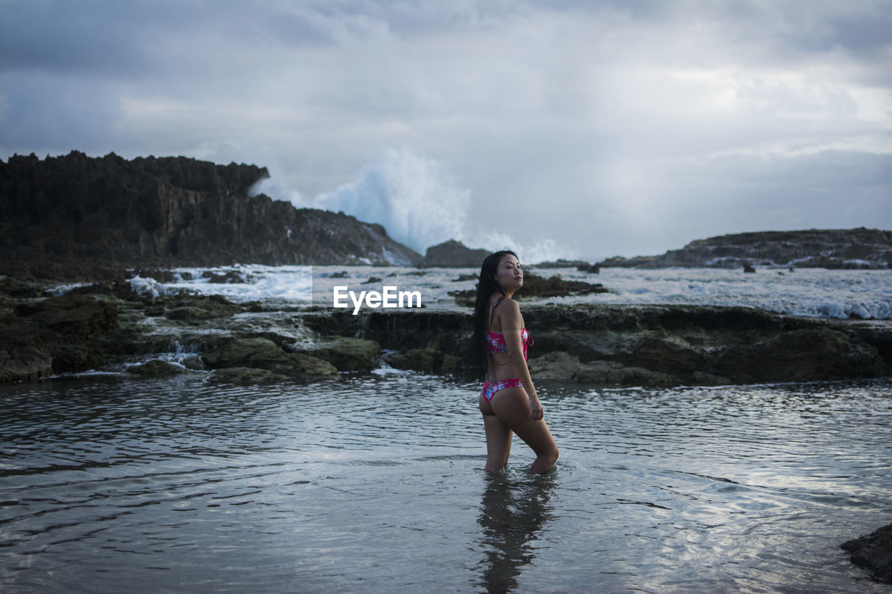 Woman stands in water on a rocky beach with tidepools