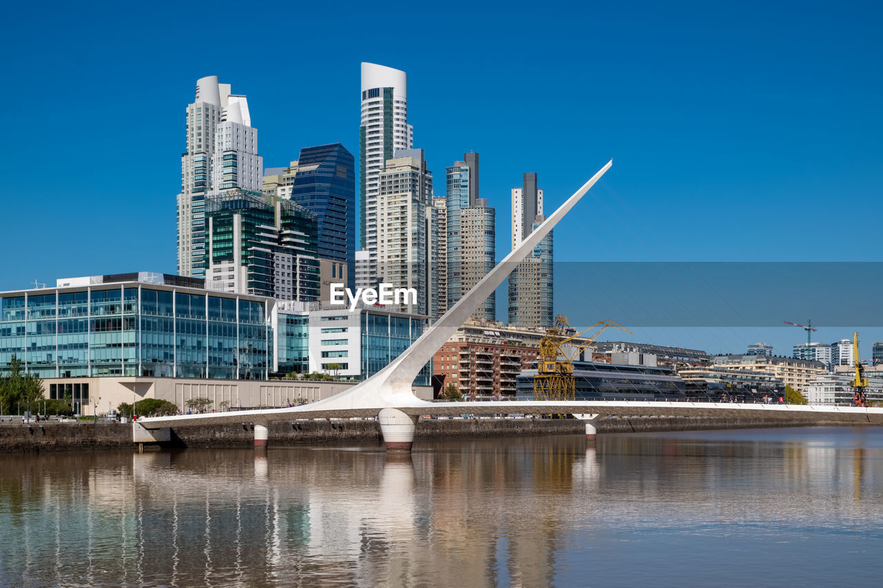 BRIDGE OVER RIVER BY BUILDINGS AGAINST SKY