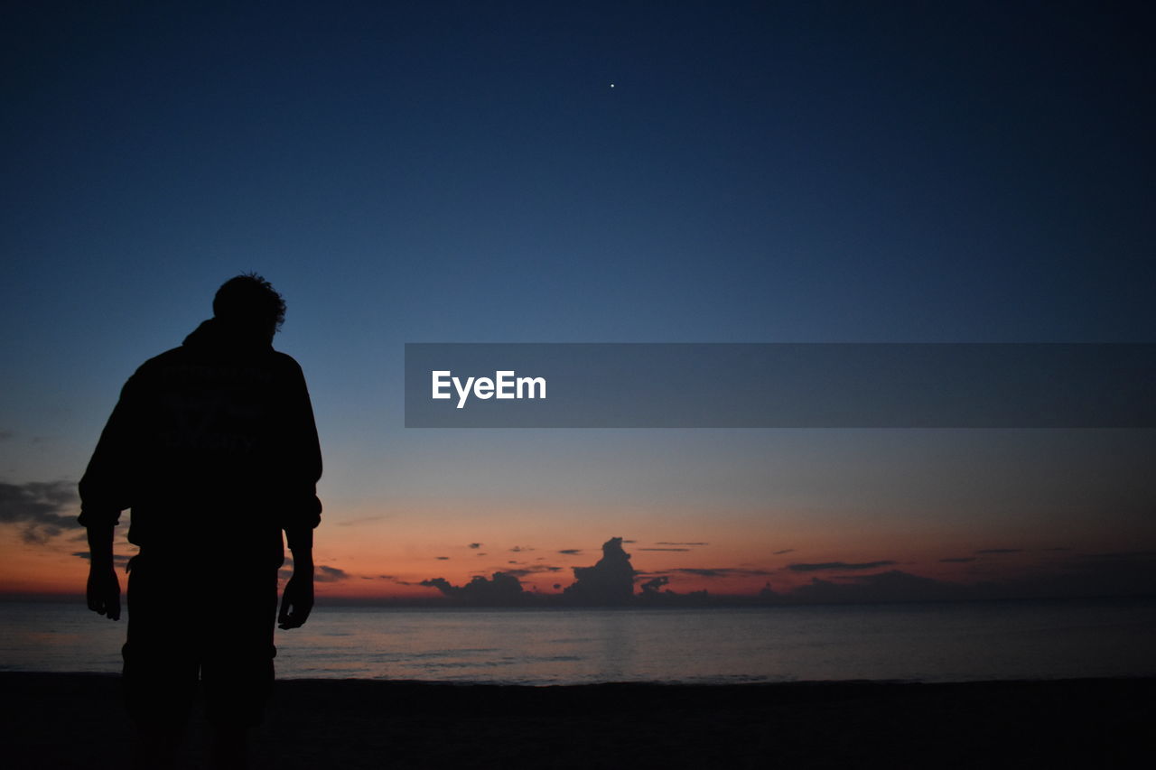 Silhouette man looking at sea against sky during sunset