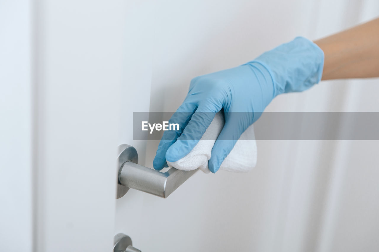 Cleaning black door handle with an antiseptic wet wipe in blue gloves. woman hand using towel 