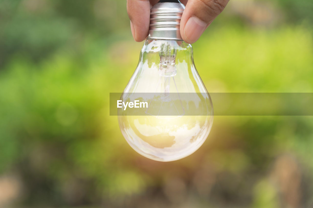 Close-up of human hand holding light bulb outdoors