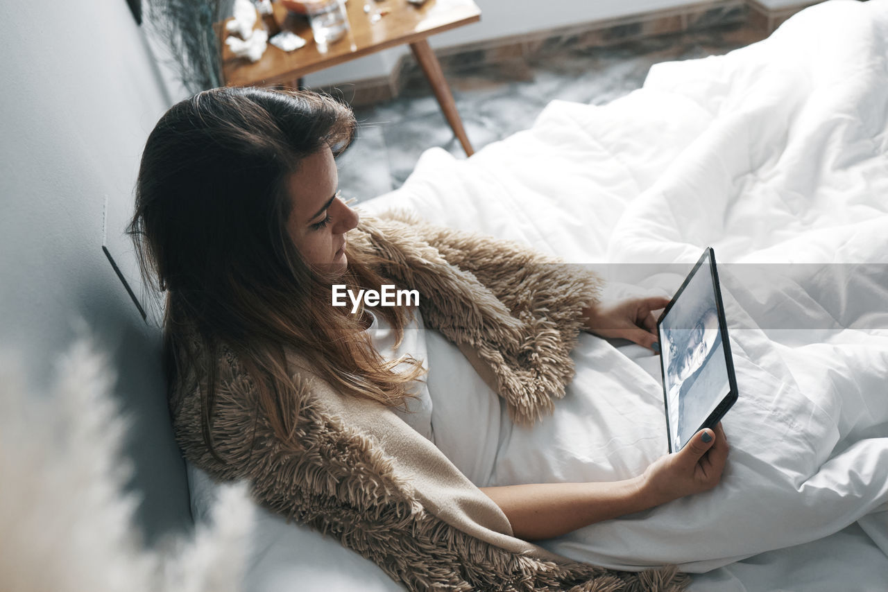 High angle view of woman using digital tablet while sitting on bed