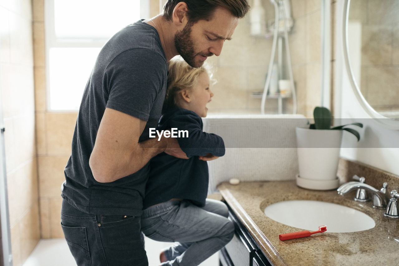 Side view of father carrying daughter at sink in bathroom