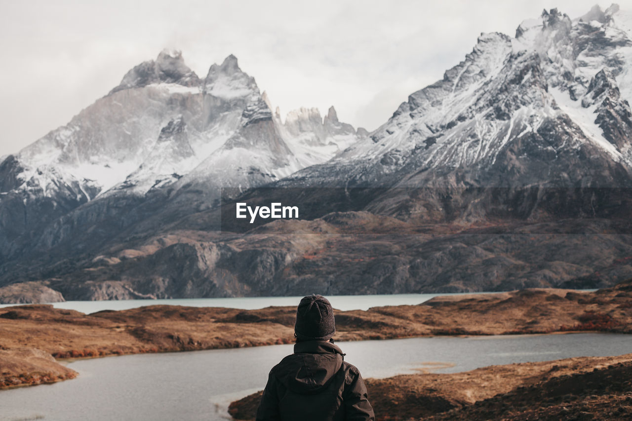 Rear view of person standing against lake and snowcapped mountains