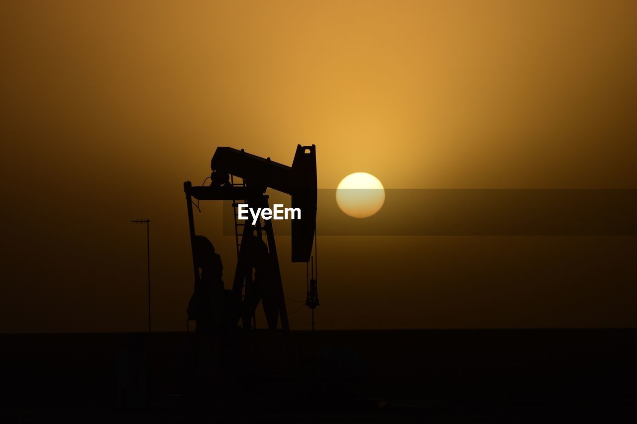 Silhouette oil well on field against sky during sunset